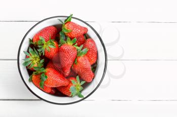 fresh ripe strawberries in a bowl on white wooden table