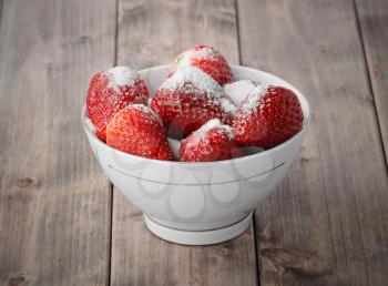 ripe strawberries in a bowl sprinkled with sugar on a wooden table
