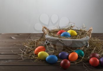 colorful easter eggs in a basket with hay and scatter of on a wooden table
