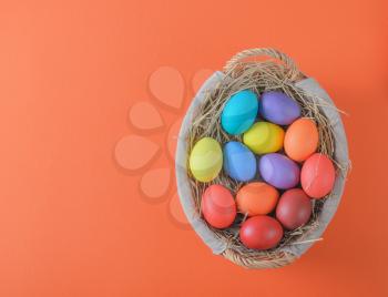 colorful easter eggs in a basket with hay on an orange background