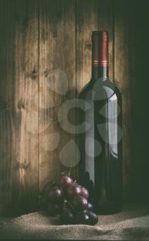 bottle of red wine with grapes on sacking and wooden background in retro style