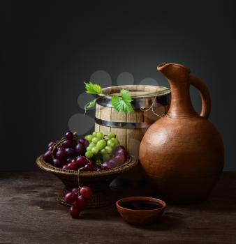 still life and cup of wine with a pitcher, a wooden barrel and grapes in a bowl