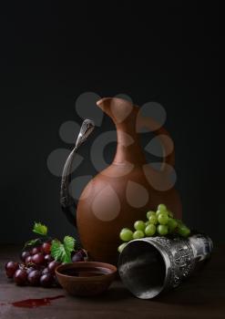 cup of wine pitcher drinking horn and grapes on a wooden table