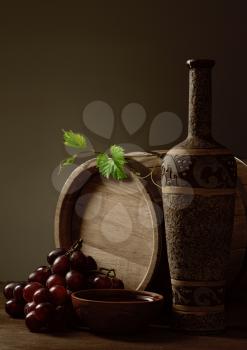 Bottle of  poured bowl wine, grapes and wooden barrel
