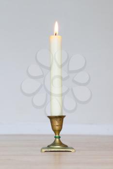 Burning candle on wooden table, white background