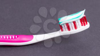 A pink toothbrush with toothpaste on a grey background