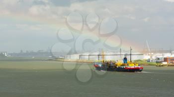 ROTTERDAM, THE NETHERLANDS - JUNE 22: Small chemical tanker sailing in the port of Rotterdam under a bright rainbow (Holland), Rotterdam, June 22, 2012