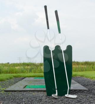 Two golf clubs standing at a driving range