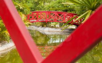 Red bridge over water in a Japanese garden, closeup of a similar bridge in the foreground