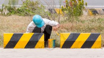 Man painting roadworks barriers on a road in Vietnam, Highway 1