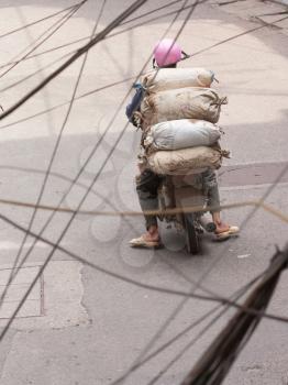 Typical Hanoi; Man with heavy load on scooter drives through Hanoi, electic wires in foreground