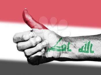 Old woman with arthritis giving the thumbs up sign, wrapped in flag pattern, Iraq