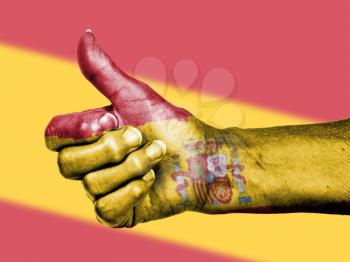 Old woman with arthritis giving the thumbs up sign, wrapped in flag pattern, Spain