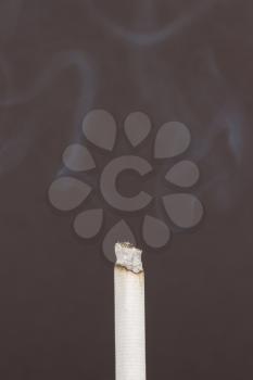 Burning cigarette with smoke on black background