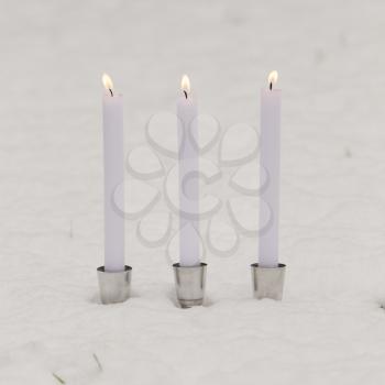 Three burning candles standing in the snow