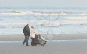Rear view of a young couple, with the female pushing a pram and walking along a beach