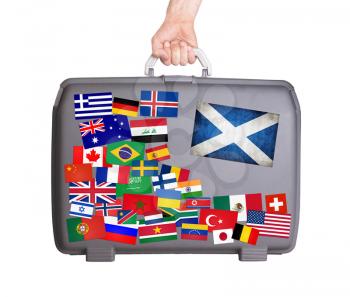 Used plastic suitcase with lots of small stickers, large sticker of Scotland