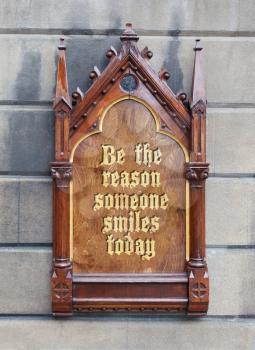 Decorative wooden sign hanging on a concrete wall - Be the reason someone smiles today