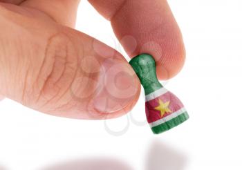 Hand holding wooden pawn with a flag painting, selective focus, Suriname