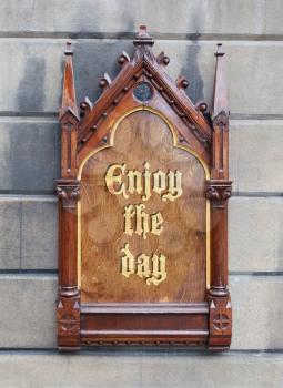 Decorative wooden sign hanging on a concrete wall - Enjoy the day