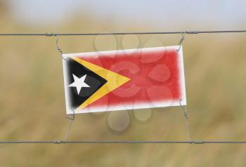 Border fence - Old plastic sign with a flag - East Timor