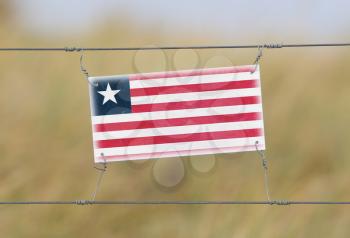 Border fence - Old plastic sign with a flag - Liberia