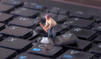Miniature worker with pickaxe working on a computer keyboard