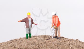 Miniature worker with a power drill on a mountain of sand