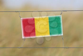 Border fence - Old plastic sign with a flag - Guinea