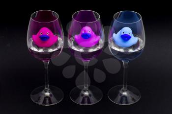 Pink, purple and blue rubber ducks in wineglasses, dark background
