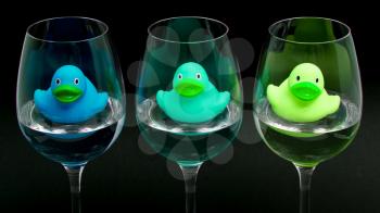 Blue and green rubber ducks in wineglasses, dark background