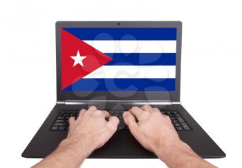 Hands working on laptop showing on the screen the flag of Cuba