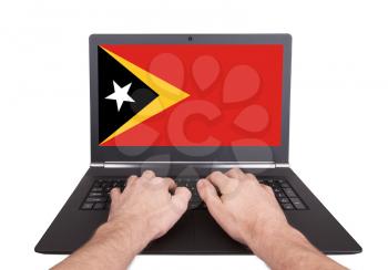 Hands working on laptop showing on the screen the flag of East Timor