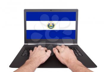 Hands working on laptop showing on the screen the flag of El Salvador