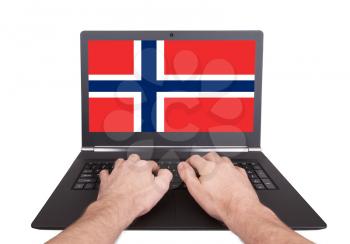 Hands working on laptop showing on the screen the flag of Norway