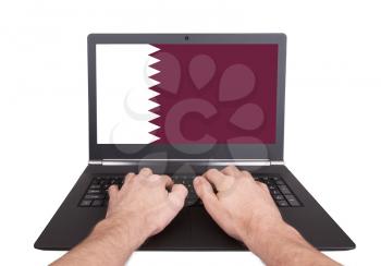 Hands working on laptop showing on the screen the flag of Qatar