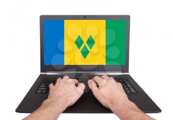 Hands working on laptop showing on the screen the flag of Saint Vincent and the Grenadines