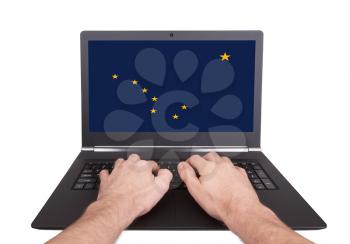 Hands working on laptop showing on the screen the flag of Alaska