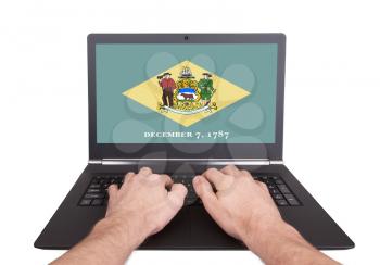 Hands working on laptop showing on the screen the flag of Delaware