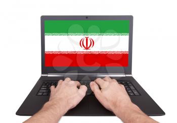 Hands working on laptop showing on the screen the flag of Iran