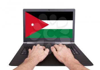 Hands working on laptop showing on the screen the flag of Jordan