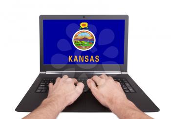 Hands working on laptop showing on the screen the flag of Kansas