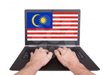 Hands working on laptop showing on the screen the flag of Malaysia