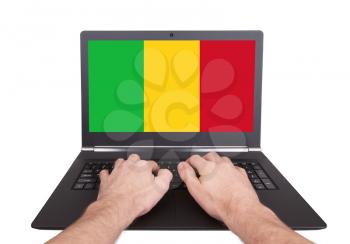 Hands working on laptop showing on the screen the flag of Mali