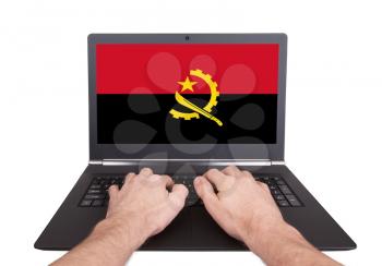Hands working on laptop showing on the screen the flag of Angola