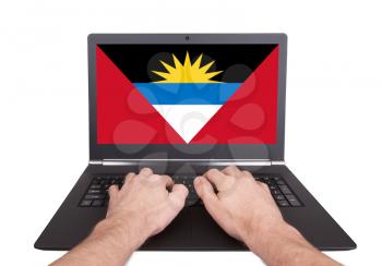 Hands working on laptop showing on the screen the flag of Antigua and Barbuda