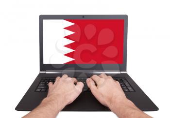 Hands working on laptop showing on the screen the flag of Bahrain