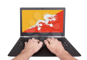 Hands working on laptop showing on the screen the flag of Bhutan