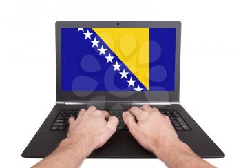 Hands working on laptop showing on the screen the flag of Bosnia and Herzegovina
