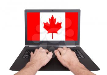 Hands working on laptop showing on the screen the flag of Canada